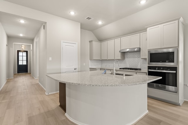 kitchen featuring stainless steel appliances, an island with sink, light stone counters, white cabinets, and lofted ceiling