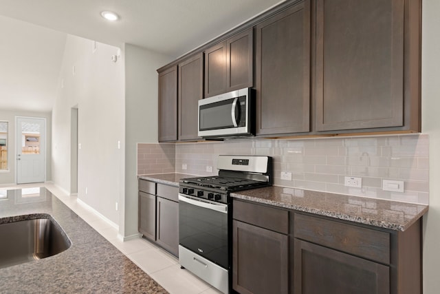 kitchen featuring stone countertops, backsplash, dark brown cabinetry, light tile patterned floors, and appliances with stainless steel finishes