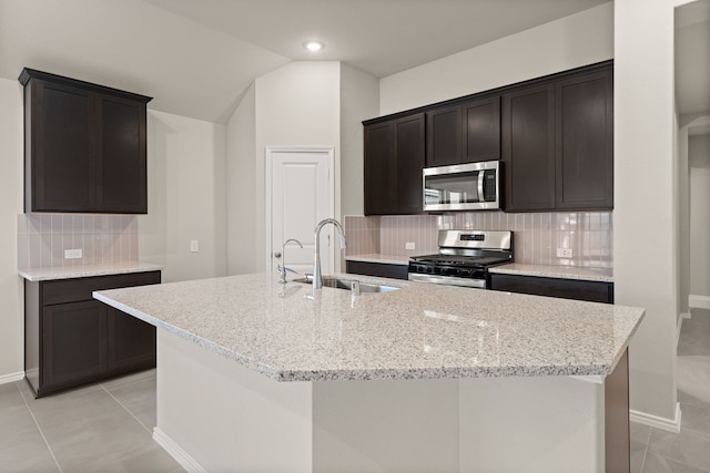 kitchen with light stone counters, stainless steel appliances, sink, and a center island with sink