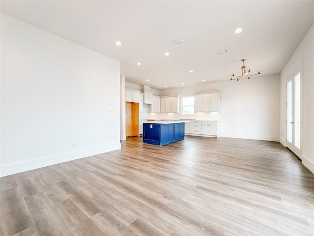 unfurnished living room with a wealth of natural light, a notable chandelier, and light hardwood / wood-style floors