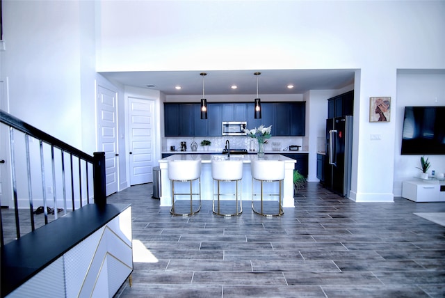 kitchen with appliances with stainless steel finishes, a kitchen bar, backsplash, decorative light fixtures, and a kitchen island with sink