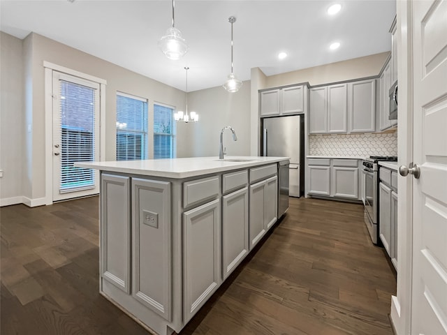 kitchen with tasteful backsplash, decorative light fixtures, stainless steel appliances, dark hardwood / wood-style floors, and an island with sink