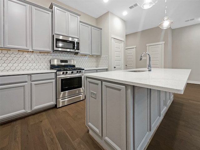 kitchen featuring appliances with stainless steel finishes, sink, dark hardwood / wood-style flooring, hanging light fixtures, and a center island with sink