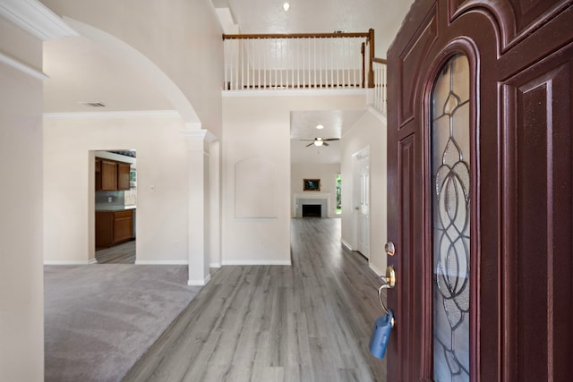 foyer entrance featuring ceiling fan, a high ceiling, decorative columns, crown molding, and light hardwood / wood-style floors