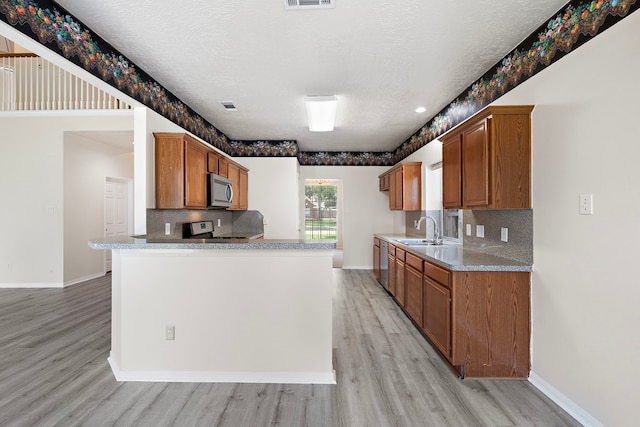 kitchen with backsplash, a textured ceiling, appliances with stainless steel finishes, and light hardwood / wood-style flooring