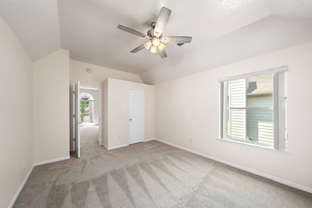 unfurnished bedroom with ceiling fan, light colored carpet, a textured ceiling, and vaulted ceiling