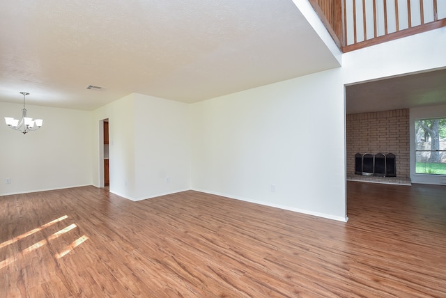 unfurnished room featuring a fireplace, brick wall, an inviting chandelier, hardwood / wood-style flooring, and a textured ceiling