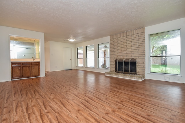 unfurnished living room with hardwood / wood-style floors, brick wall, a fireplace, and a textured ceiling