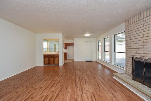 unfurnished living room with wood-type flooring, a fireplace, brick wall, sink, and a textured ceiling