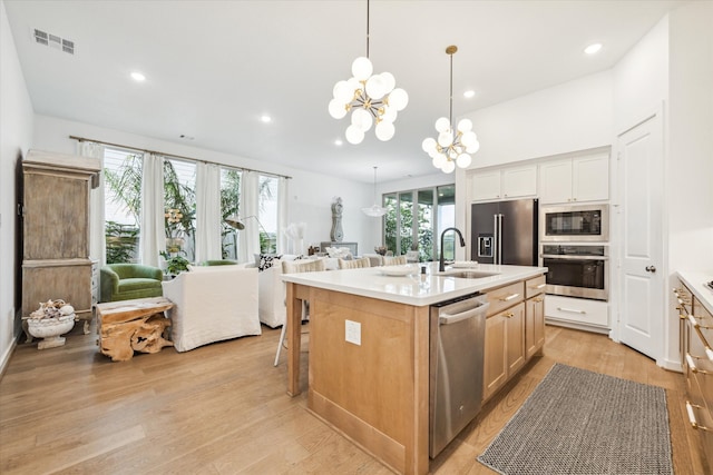 kitchen with stainless steel appliances, light hardwood / wood-style floors, a center island with sink, sink, and an inviting chandelier