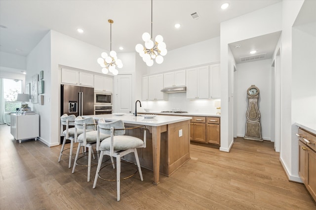 kitchen with light hardwood / wood-style flooring, tasteful backsplash, a chandelier, stainless steel appliances, and a center island with sink