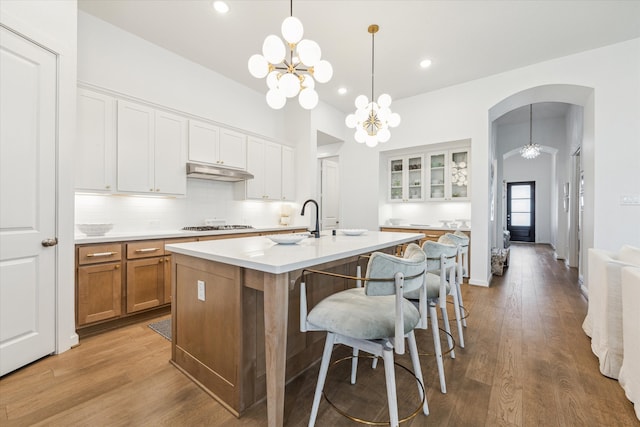 kitchen with white cabinetry, backsplash, a chandelier, a center island with sink, and hardwood / wood-style flooring