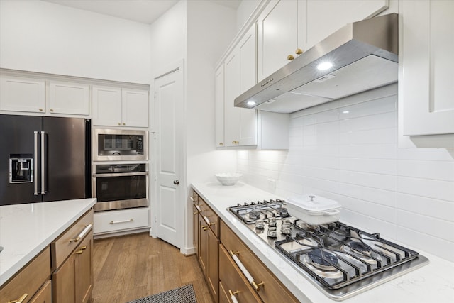 kitchen with white cabinetry, appliances with stainless steel finishes, backsplash, light stone counters, and light wood-type flooring