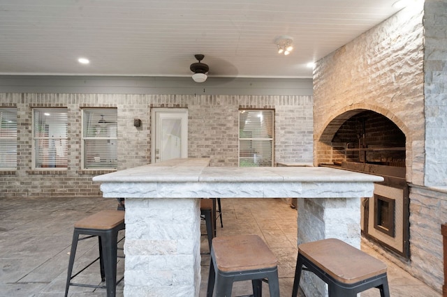 kitchen featuring a breakfast bar, brick wall, light tile flooring, and ceiling fan