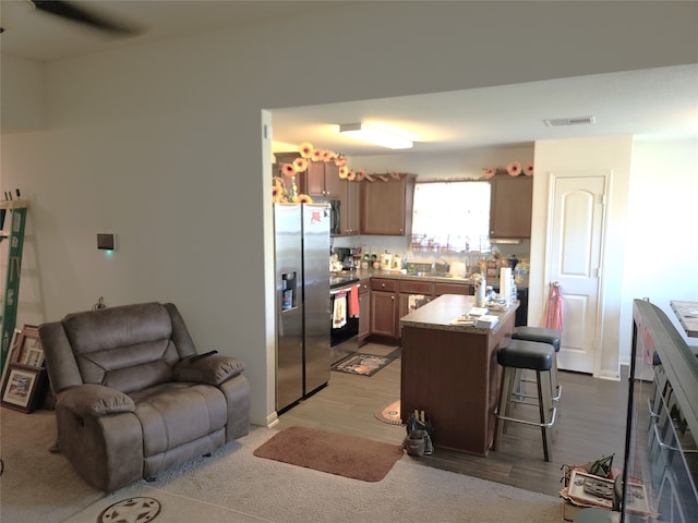 kitchen featuring wood-type flooring, stainless steel refrigerator with ice dispenser, range, sink, and a breakfast bar