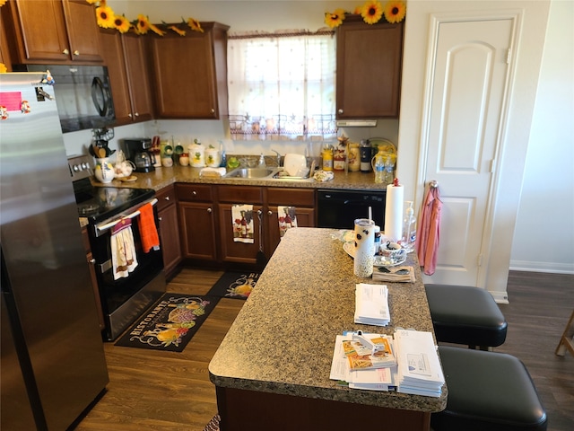 kitchen featuring a breakfast bar, dark wood-type flooring, black appliances, sink, and a kitchen island