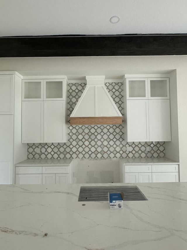 interior space featuring premium range hood, light stone countertops, decorative backsplash, and white cabinetry