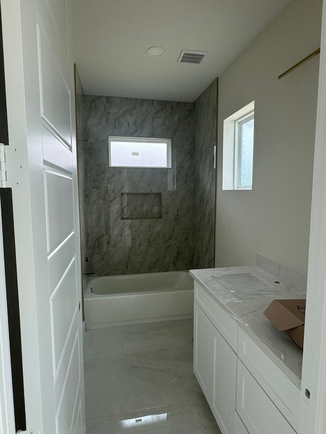 bathroom with tiled shower / bath, vanity, and a healthy amount of sunlight