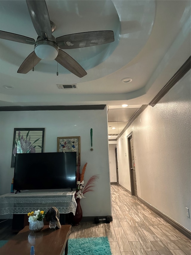 living room featuring ornamental molding, light hardwood / wood-style floors, ceiling fan, and a tray ceiling