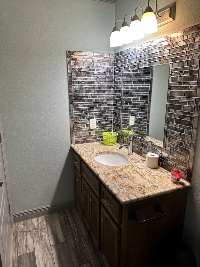 bathroom featuring wood-type flooring, vanity with extensive cabinet space, tasteful backsplash, and crown molding