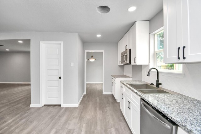 kitchen featuring appliances with stainless steel finishes, light hardwood / wood-style flooring, white cabinets, sink, and light stone counters