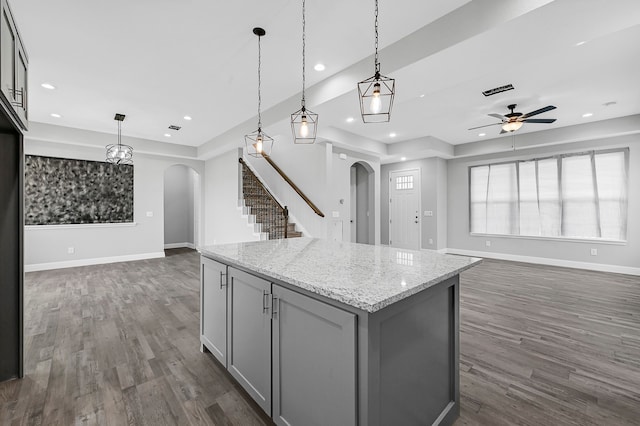 kitchen featuring light stone countertops, a kitchen island, pendant lighting, and dark wood-type flooring