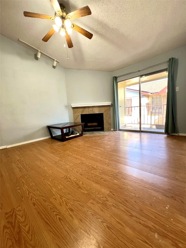 unfurnished living room featuring ceiling fan, a tile fireplace, a textured ceiling, hardwood / wood-style floors, and track lighting