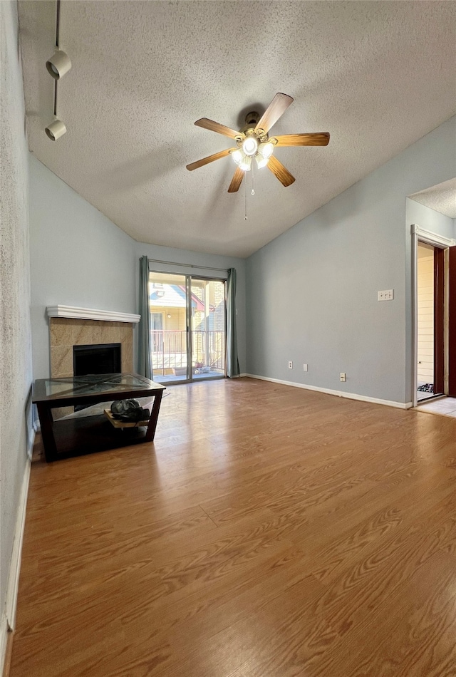 unfurnished living room with rail lighting, hardwood / wood-style flooring, a tiled fireplace, and a textured ceiling