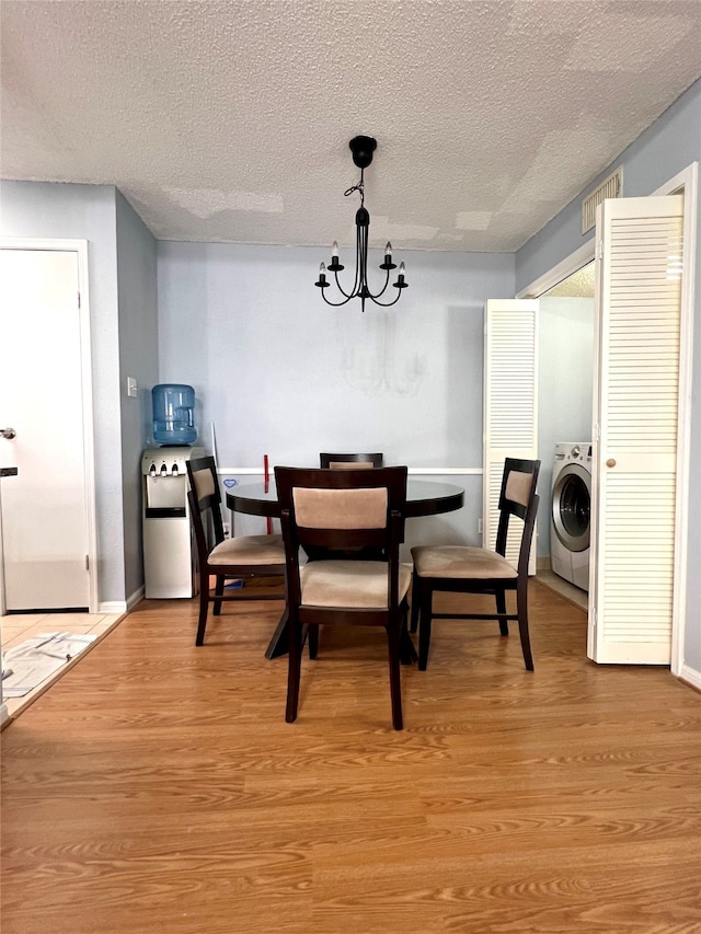 dining space with an inviting chandelier, washer / dryer, light hardwood / wood-style floors, and a textured ceiling