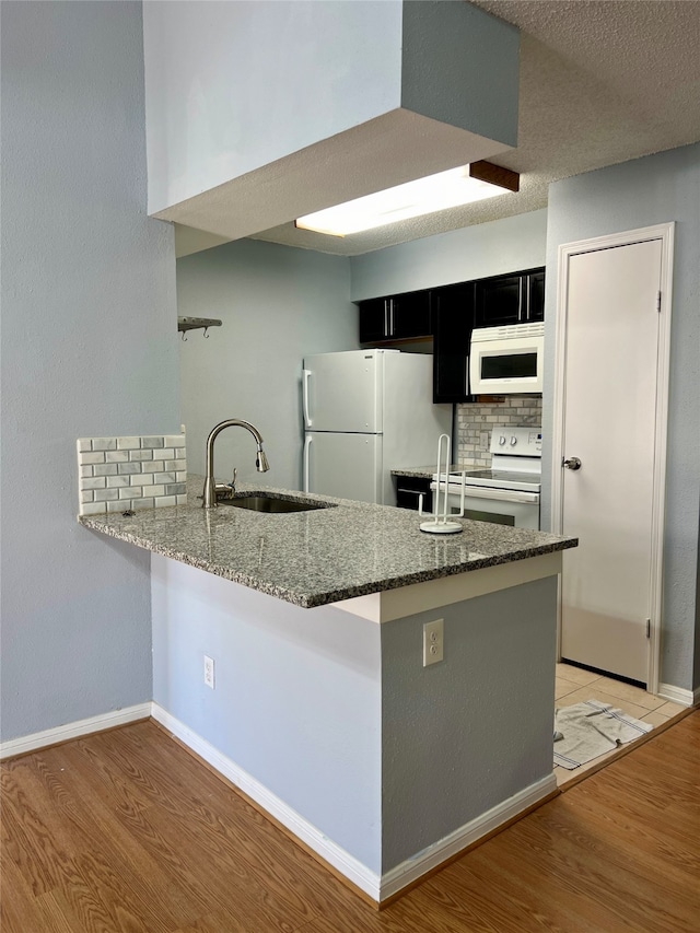 kitchen with white appliances, backsplash, kitchen peninsula, light tile floors, and sink