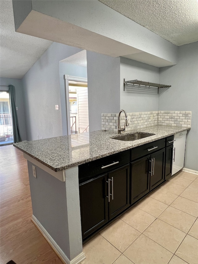 kitchen with tasteful backsplash, kitchen peninsula, sink, and light stone counters