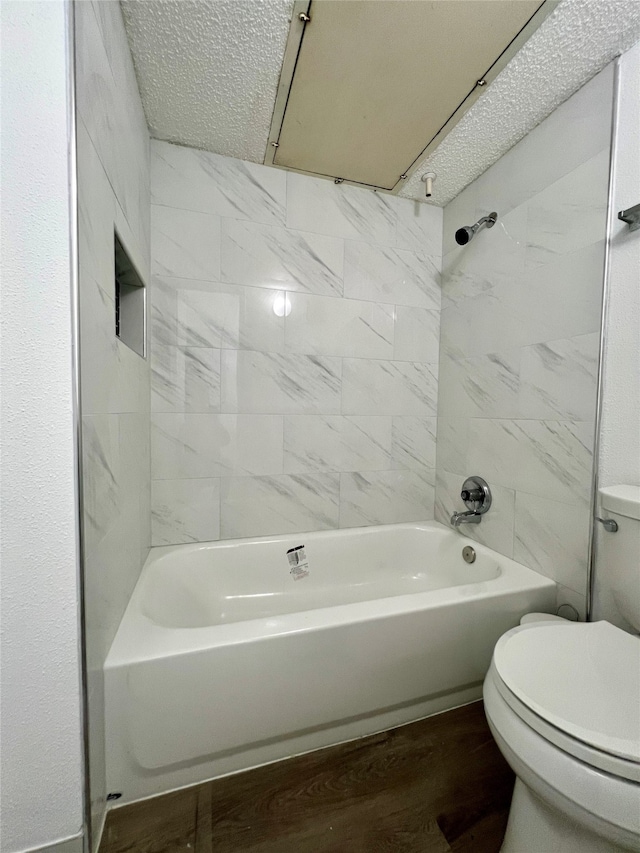 bathroom featuring wood-type flooring, tiled shower / bath, toilet, and a textured ceiling