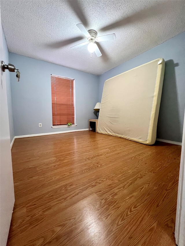 unfurnished bedroom featuring ceiling fan, hardwood / wood-style flooring, and a textured ceiling