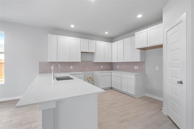 kitchen with white cabinetry, kitchen peninsula, sink, and light hardwood / wood-style floors