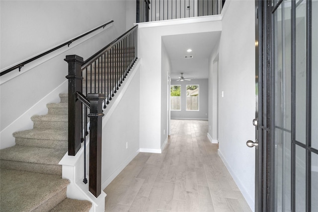 foyer entrance featuring ceiling fan, a high ceiling, wood finished floors, baseboards, and stairs