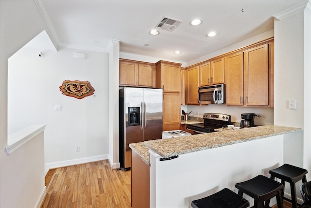 kitchen featuring light stone countertops, kitchen peninsula, appliances with stainless steel finishes, light hardwood / wood-style floors, and a breakfast bar