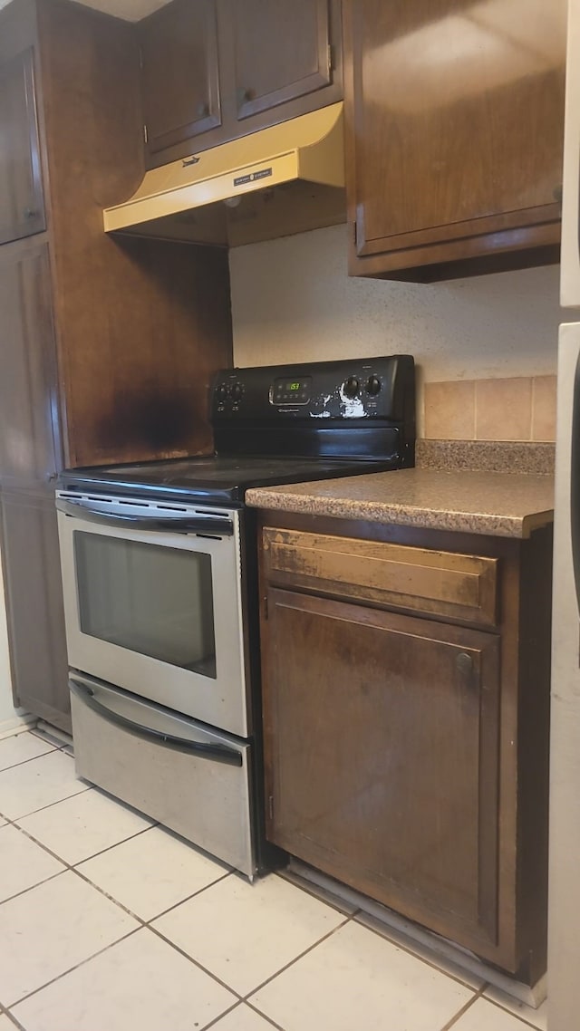 kitchen featuring electric range, dark brown cabinets, and light tile floors