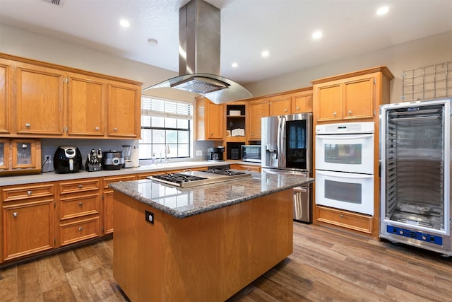 kitchen featuring wood-type flooring, island exhaust hood, appliances with stainless steel finishes, a kitchen island, and dark stone countertops