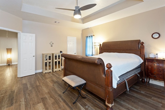 bedroom with ceiling fan, a raised ceiling, and dark wood-type flooring