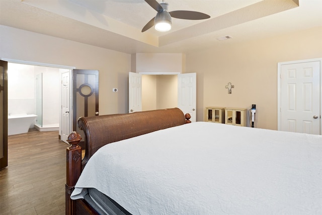 bedroom featuring ceiling fan, a tray ceiling, hardwood / wood-style flooring, and connected bathroom