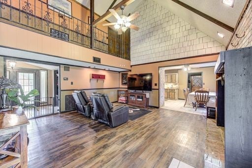 living room featuring high vaulted ceiling, wood-type flooring, ceiling fan, and beam ceiling