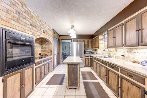 kitchen featuring sink, a center island, light tile flooring, and backsplash