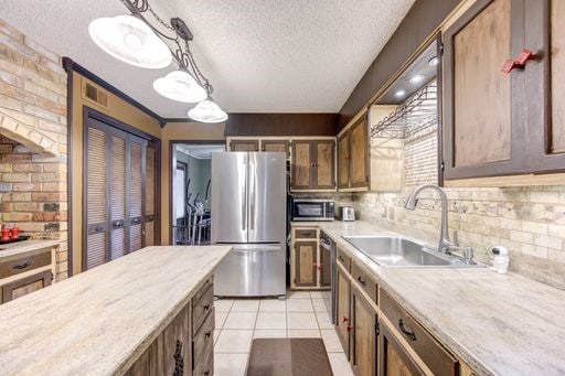 kitchen with pendant lighting, light tile flooring, appliances with stainless steel finishes, sink, and tasteful backsplash