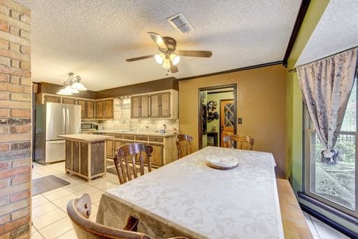 tiled dining space with a textured ceiling, ceiling fan, brick wall, and ornamental molding