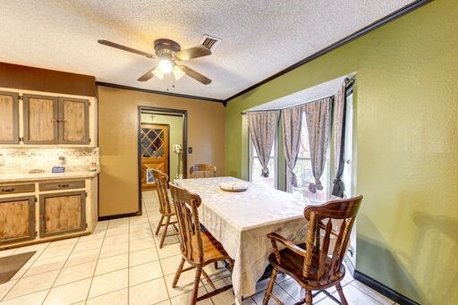 dining area with light tile floors, ornamental molding, ceiling fan, and a textured ceiling