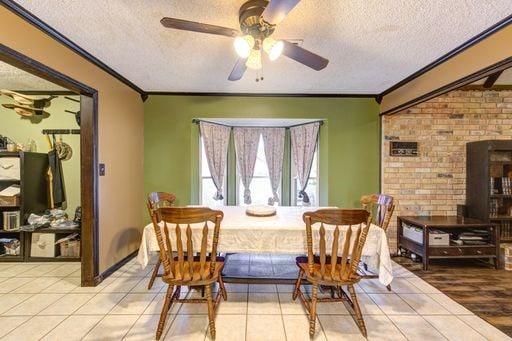 dining area with tile flooring, brick wall, ceiling fan, and a textured ceiling