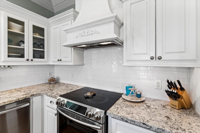 kitchen featuring white cabinets, tasteful backsplash, stainless steel appliances, premium range hood, and light stone countertops