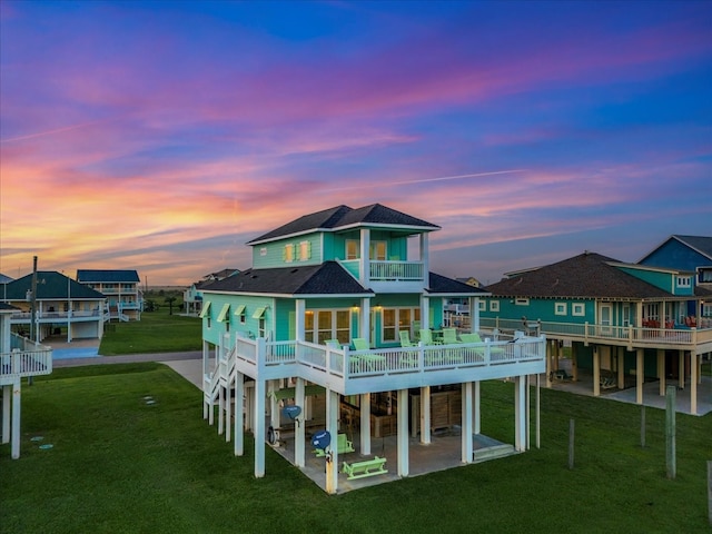 back house at dusk with a patio area, a yard, and a balcony