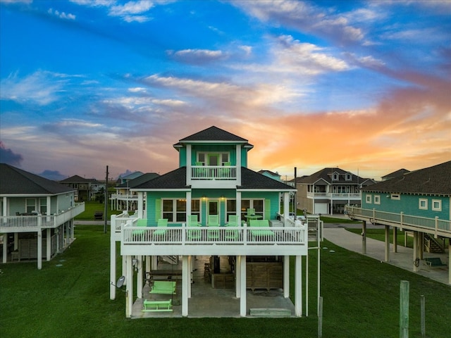 back house at dusk with a patio, a balcony, and a lawn