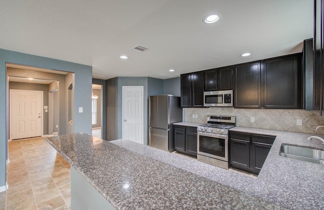 kitchen featuring stainless steel appliances, backsplash, light stone countertops, sink, and light tile floors